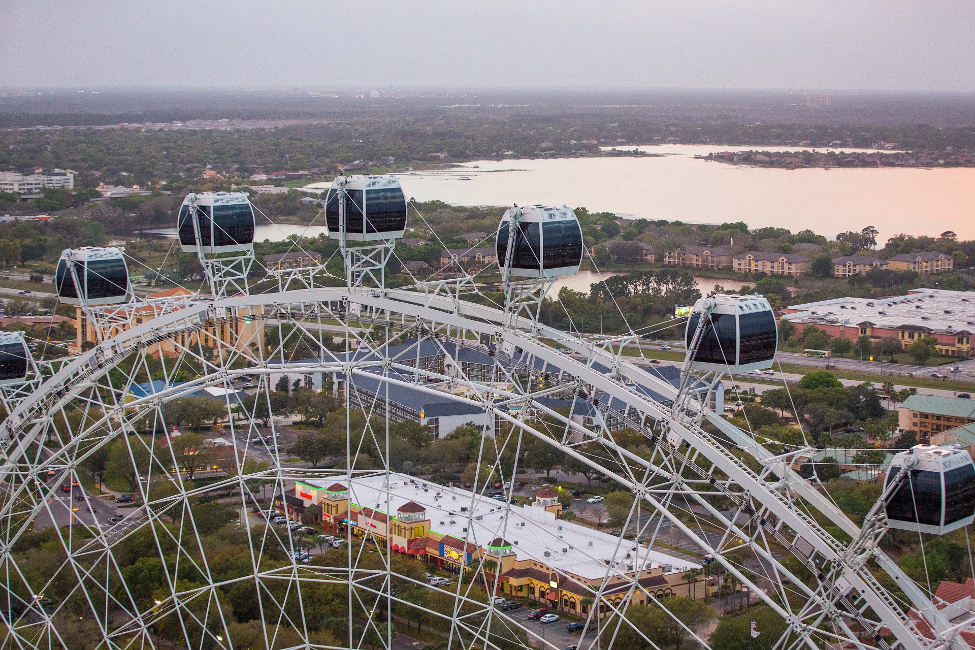 Several capsules of The Orlando Eye in the foreground with a lake in the background. The sun is also setting.