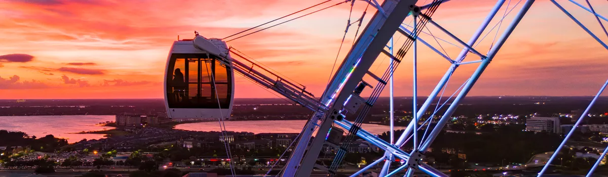 Drone view of an Orlando Eye capsule at dusk with International Drive in the background.