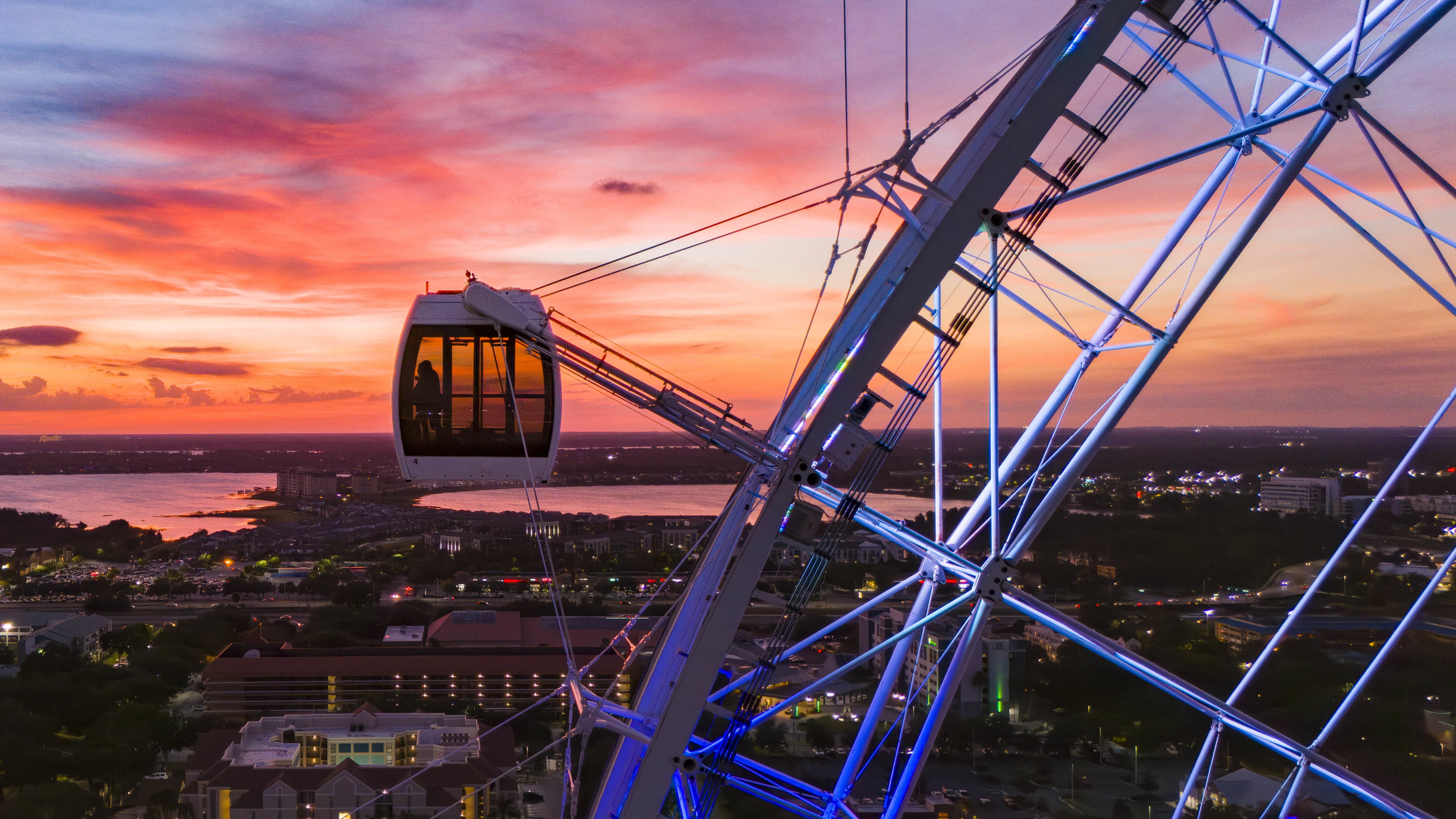 Drone view of an Orlando Eye capsule at dusk with International Drive in the background.